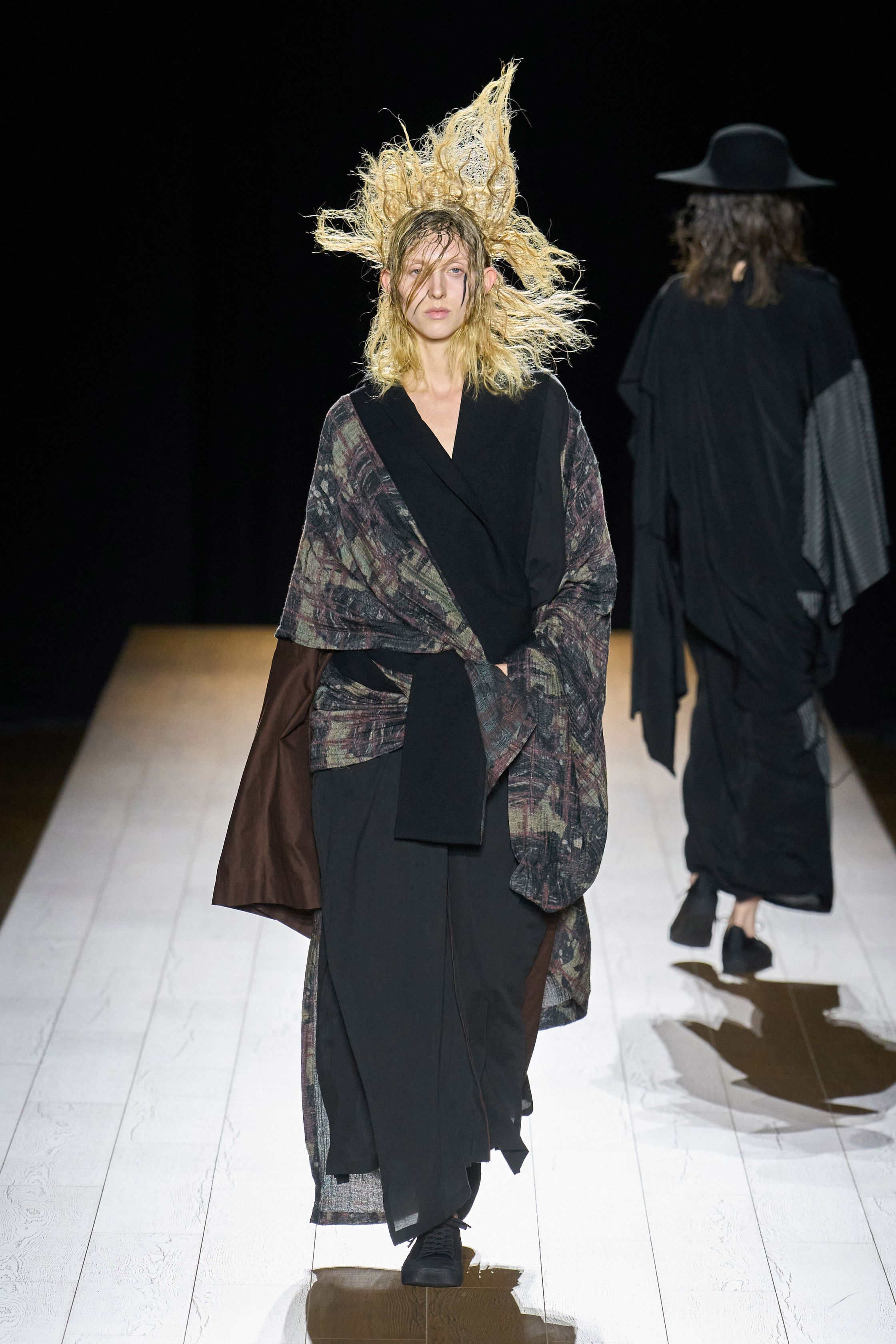 Yohji Yamamoto 本季依然延续标志性的黑色哲学：宽松层叠轮廓、和服式结构与手工拼接面料形成一种诗意而深沉的东方美学。夸张头饰与飘逸衣摆让整场秀像一场黑色戏剧，既神秘又极具艺术感-顽石频道趋势研究